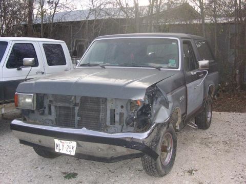 1990 Ford Bronco - A damaged Ford Bronco sits parked next to a white truck.