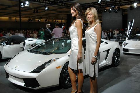 1991 Ford Taurus - Two women stand next to a white Lamborghini Gallardo at an auto show, with another Lamborghini visible in the background.