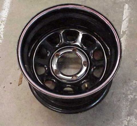 1976 Jeep CJ7 - A close-up view of a black steel wheel with a silver trim ring is shown against a concrete surface.
