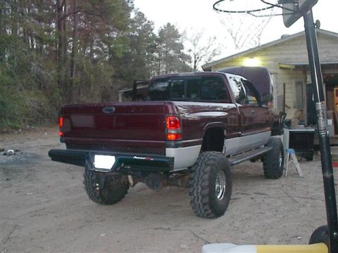 2001 Dodge 1500 - A maroon pickup truck with a lifted suspension and large off-road tires is parked outdoors with its hood up.