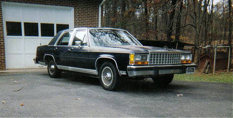 Dark blue Ford LTD Crown Victoria sedan parked in a driveway, front three-quarter view