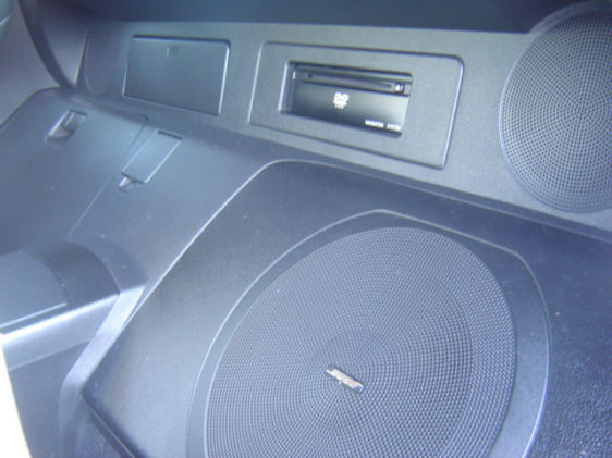 Rear cargo area with a large round subwoofer in a black molded enclosure and CD unit