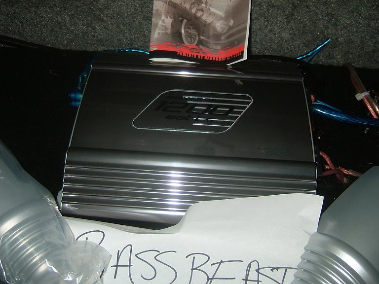 Car audio amplifier with '1200' watts visible, on a carpeted surface
