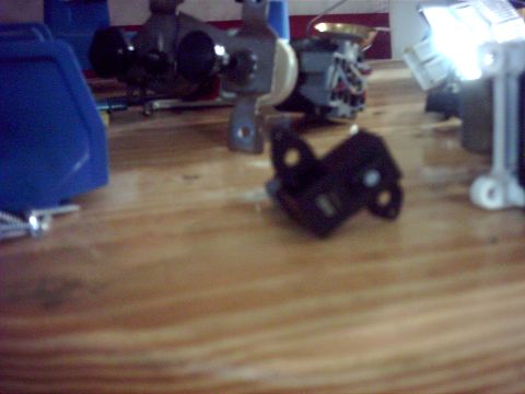 1996 Ford Bronco - A black metal bracket is shown on a wooden surface, with other parts blurred in the background.