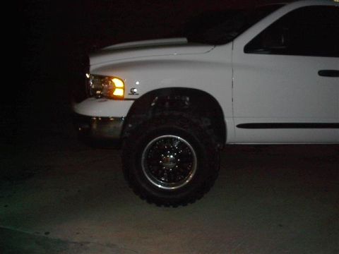 2001 Dodge 1500 - Front corner of a white 2001 Dodge 1500 pickup truck, showing the headlight, grille, and wheel.