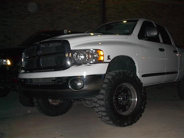 Lifted white Dodge pickup truck with large tires, parked next to another vehicle