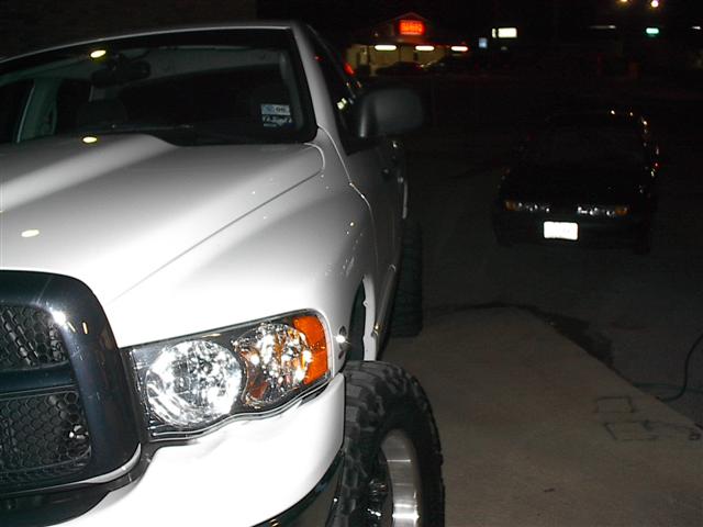 White pickup truck parked at night, another car in background. License plate visible on truck