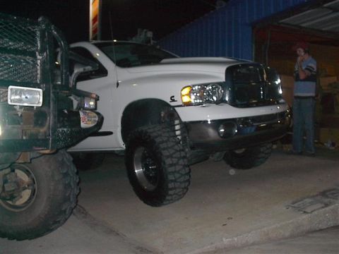 2001 Dodge 1500 - A white 2001 Dodge Ram 1500 pickup truck is parked next to another vehicle, showing its front 3/4 view with prominent off-road tires.