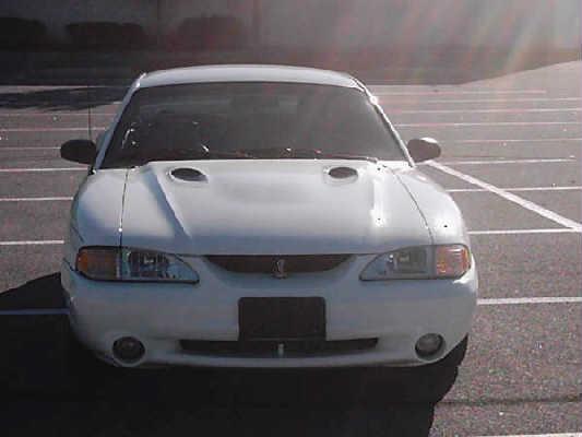 Front of white Mustang SVT Cobra with twin hood scoops and round foglights in an empty parking lot