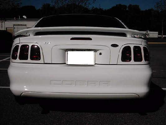 Rear of white Mustang Cobra coupe with COBRA bumper lettering, SVT trunk badge and red taillights