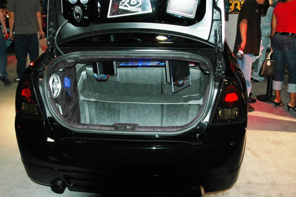 Black car trunk open, showing custom audio setup with speakers and blue lighting