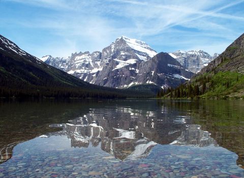 1996 Ford Bronco - A vast mountain range reflects in a clear lake, with a rocky shoreline in the foreground.