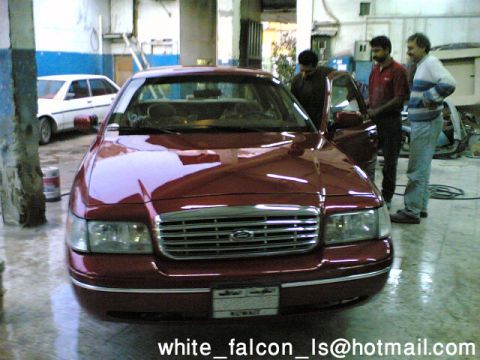 1999 Mercury Grand Marquis - A red sedan with a Ford emblem on its grille is shown from the front, with a white car in the background.