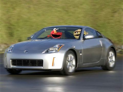 1990 Ford Probe - A silver Nissan 350Z drives down the road with Elmo and Oscar the Grouch puppets visible in the windows.