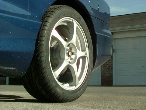 1995 Ford Probe - Close-up of a blue car's rear quarter panel and a five-spoke alloy wheel, with a garage door visible in the background.