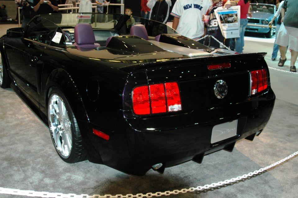 Black convertible sports car with purple interior, rear view, custom wheels, spoiler, and aftermarket exhaust