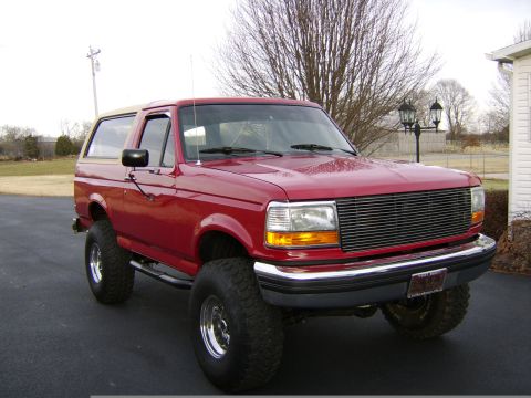 1989 Ford Bronco - This red Ford Bronco is modified with a lift kit and large tires, a tan removable top.