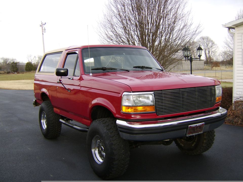 Red lifted Ford Bronco with tan top and billet grille parked on driveway, three-quarter front view