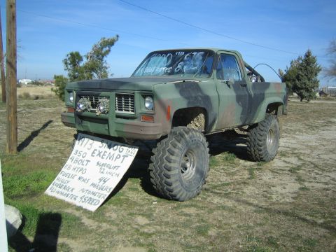 1990 Ford Bronco - lifted camouflage-painted square-body pickup on oversized tires displayed outdoors with a handwritten for-sale spec sign.