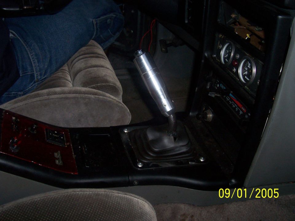 Car interior with tall aluminum manual shifter, black boot, aftermarket gauges and gray cloth seats