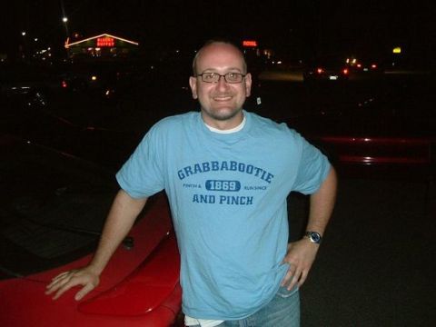 1995 Ford Probe - A man stands next to the fender and spoiler of a red car at night.