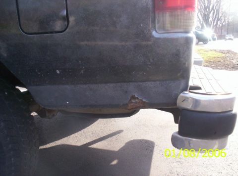 1988 Ford Bronco - Close-up of a rusted rear bumper on a dark-colored SUV, with a chrome step bumper visible to the right.