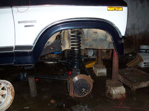 1983 Ford Bronco - The front suspension of a Ford Bronco is shown with the wheel removed and the vehicle supported by jack stands.