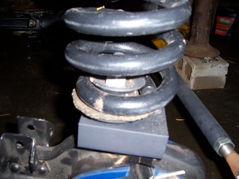 1983 Ford Bronco - Close-up view of a vehicle's suspension coil spring and an adapter block, likely part of a modification.