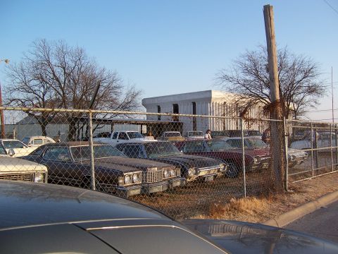 1979 Ford Ranchero - Several cars are parked in an outdoor lot behind a chain-link fence under a clear sky.