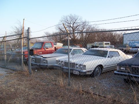 1979 Ford Ranchero - Several vehicles are parked in an outdoor lot behind a chain-link fence under a clear sky.