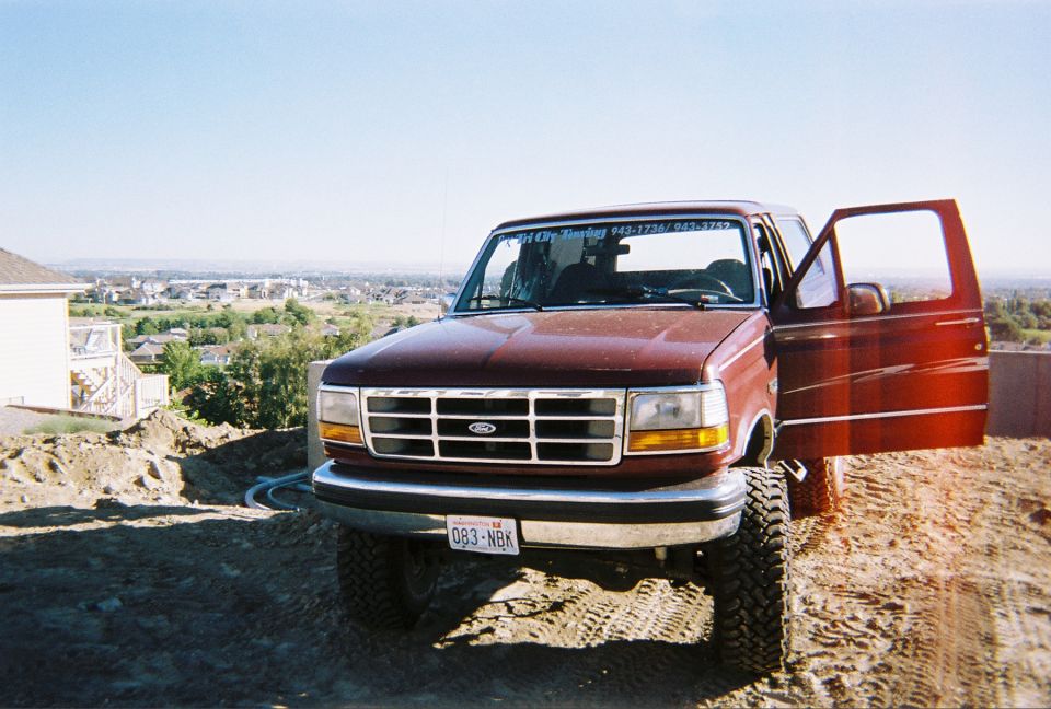 Red Ford F-Series truck with front doors open, parked on a dirt hill