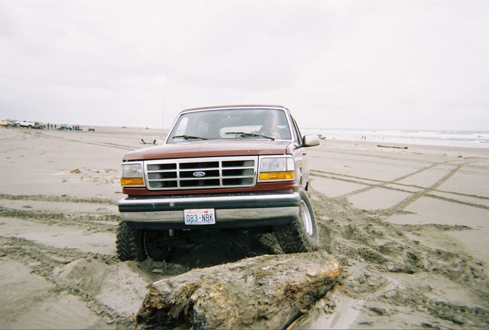 Dark red lifted Ford Bronco front view straddling driftwood on a sandy beach