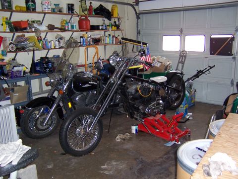 1979 Ford Ranchero - A black cruiser and a chopper are parked side-by-side in a garage filled with shelves of supplies and tools.