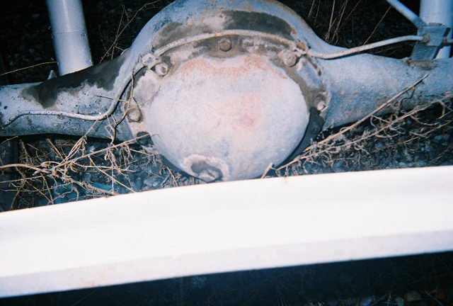 close-up of a rusty rear axle differential with some dry grass around it