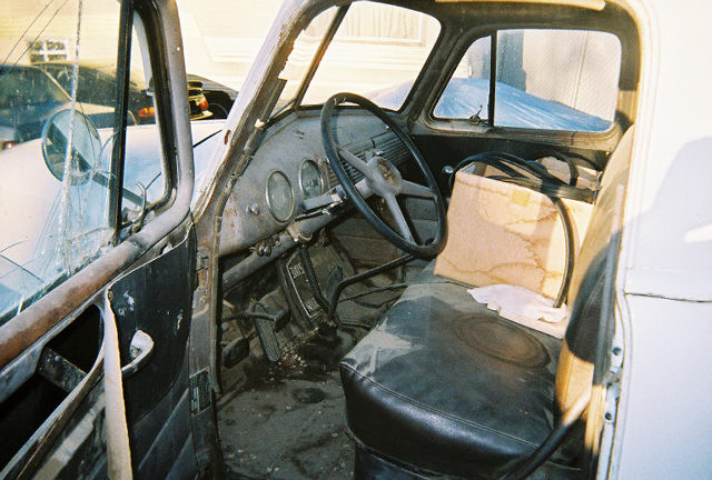 Interior of an old truck, showing cracked dashboard, worn steering wheel, and torn seat