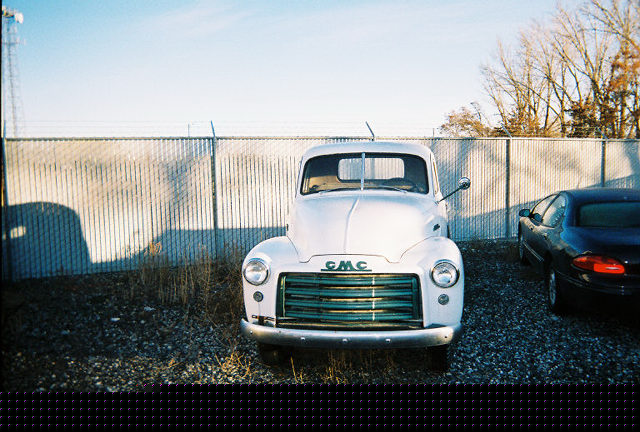 White 1950s GMC pickup truck parked next to a dark sedan