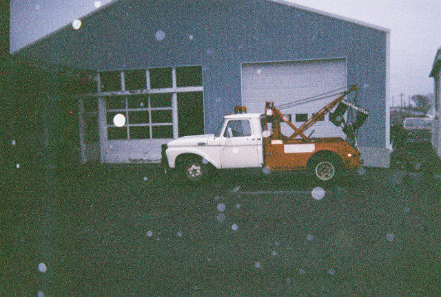 White and orange tow truck parked in front of a garage
