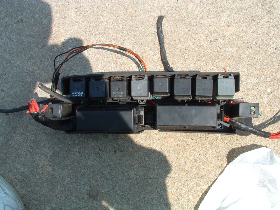 Removed relay and fuse box assembly with multiple relays and wiring harness laid on concrete