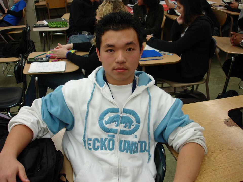Student wearing a white and blue Ecko Unltd. hoodie sits at a desk in a classroom