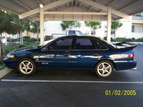 1993 Ford Taurus - Side view of a 1993 Ford Taurus sedan with custom wheels and a spoiler.