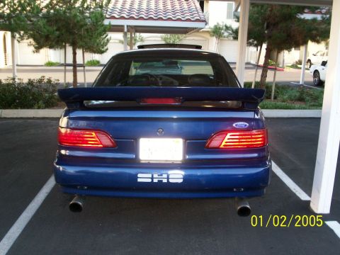 1993 Ford Taurus - The rear of a blue 1993 Ford Taurus SHO is parked in a carport. The car has a spoiler and dual exhaust pipes.