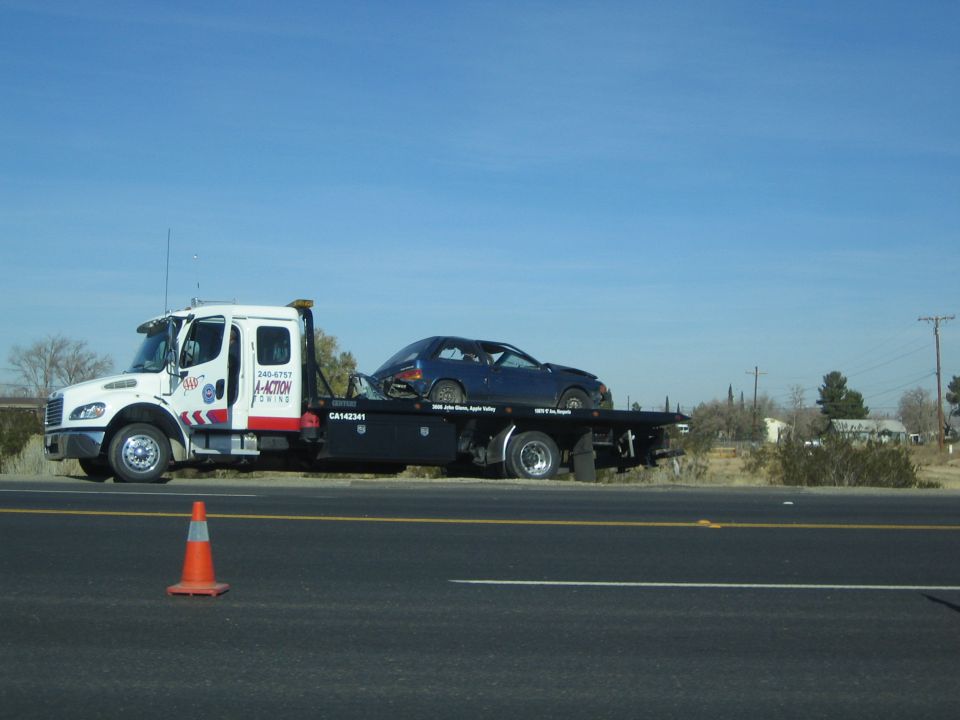 White flatbed tow truck hauling a blue sports car along a desert highway
