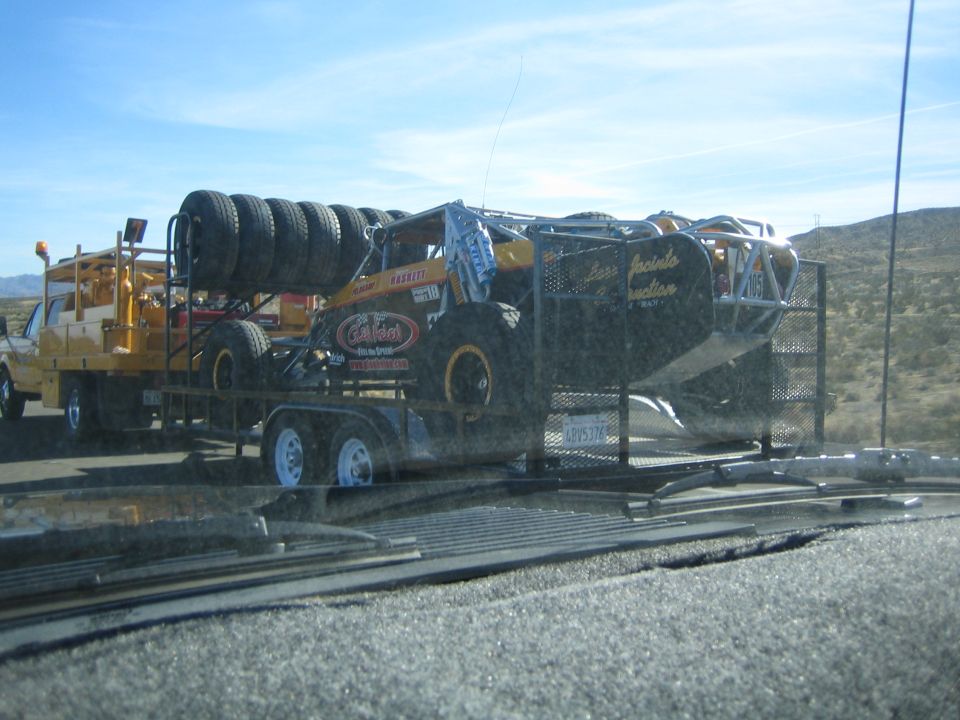 Yellow tube-chassis off-road race car loaded on a trailer behind a truck