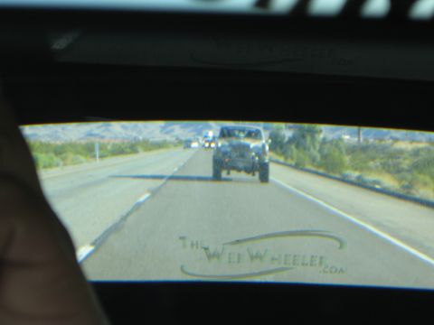 1990 Ford Bronco - Through a tinted rear window bearing TheWebWheeler.com branding, a Jeep follows behind on a desert highway.