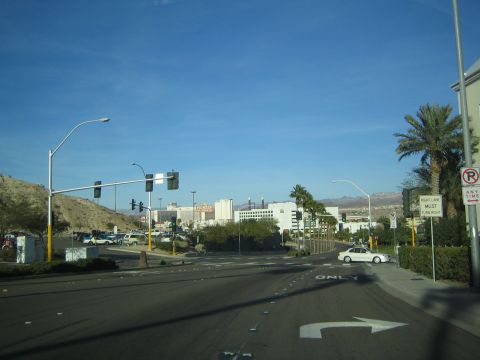 1990 Ford Bronco - wide road intersection in a desert town with casino-style buildings, palm trees, and a white car turning under clear blue sky.