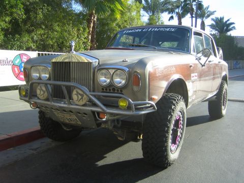 1990 Ford Bronco - lifted vintage Rolls-Royce converted into an off-road build, fitted with a tube bumper and oversized tires, parked by palms.