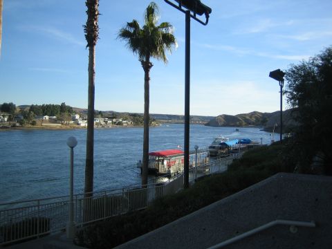 1990 Ford Bronco - calm river lined with palm trees and a railed walkway, with a docked riverboat and distant hills under a clear evening sky.