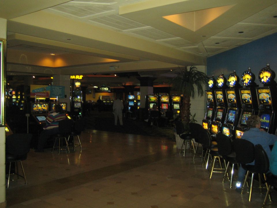 Dimly lit casino interior with rows of illuminated slot machines and seated patrons