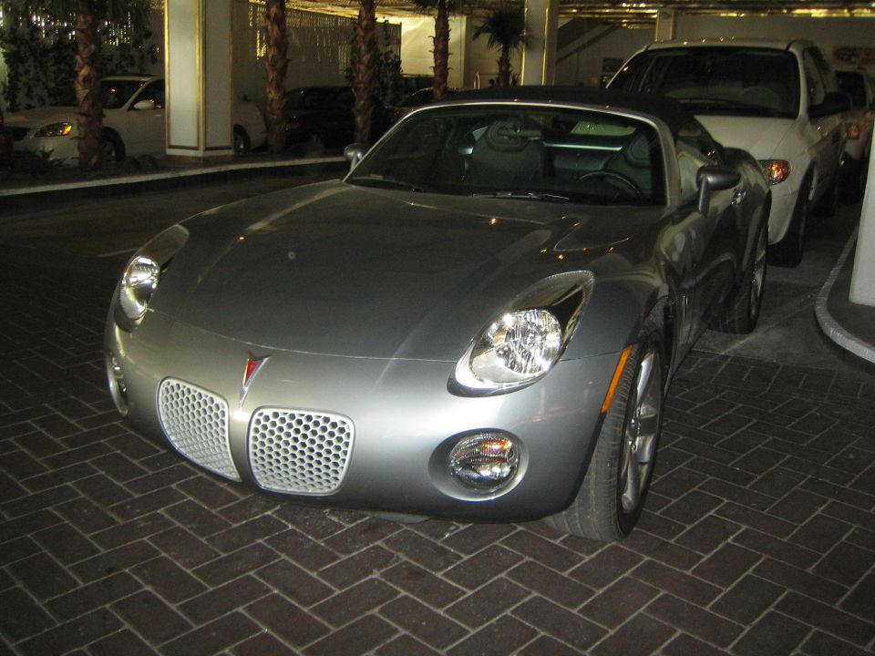 Front three-quarter view of a silver Pontiac Solstice convertible parked on brick pavers