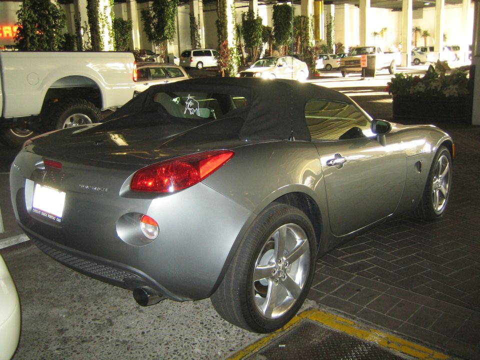 Rear three-quarter view of a gray Pontiac Solstice convertible with black soft top up